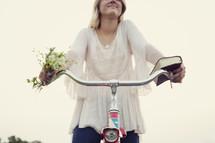 woman with flowers and a book holding onto handle bars of a bike