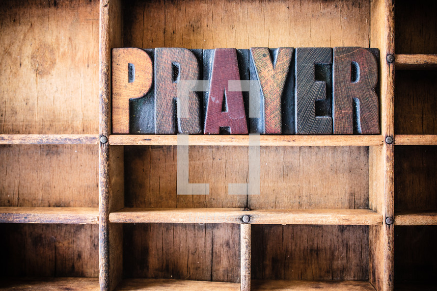 Wooden letters spelling "prayer" on a wooden bookshelf.
