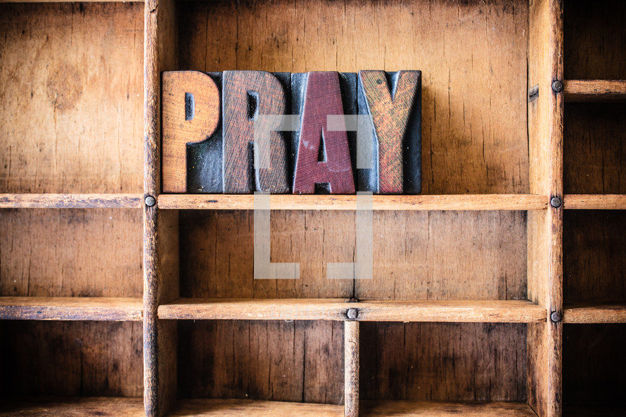 Wooden letters spelling "pray" on a wooden bookshelf.