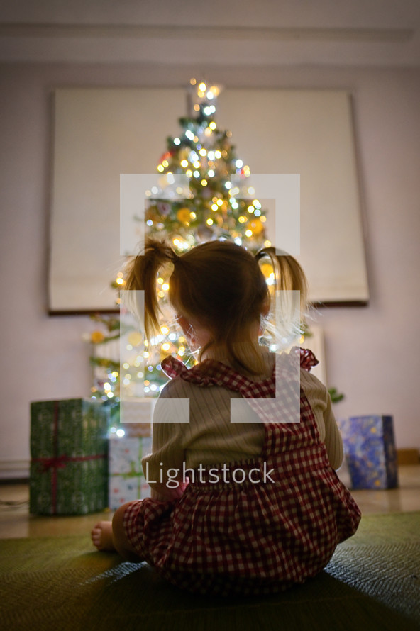 A Little Girl Looking At Christmas Tree At Home