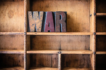 Wooden letters spelling "war" on a wooden bookshelf.