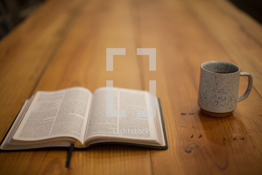 An open Bible and coffee mug on a wooden table 