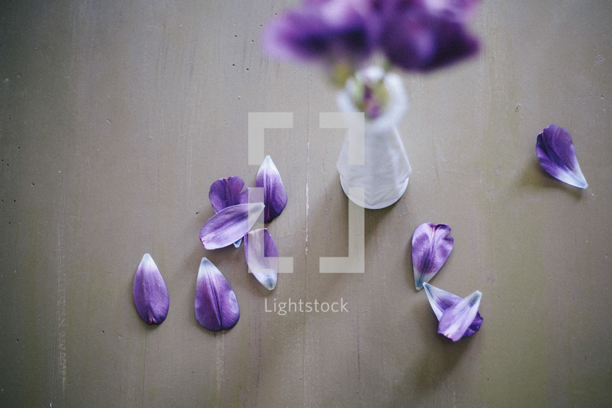 Tulips in a milk glass vase with petals on the table.
