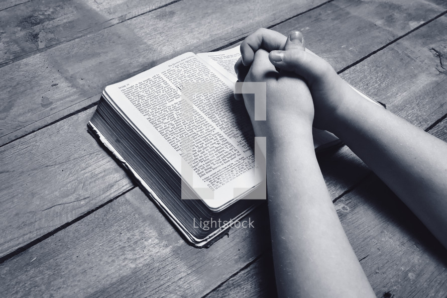 child with praying hands over a Bible 