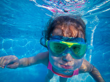 little girl with goggles under water swimming 