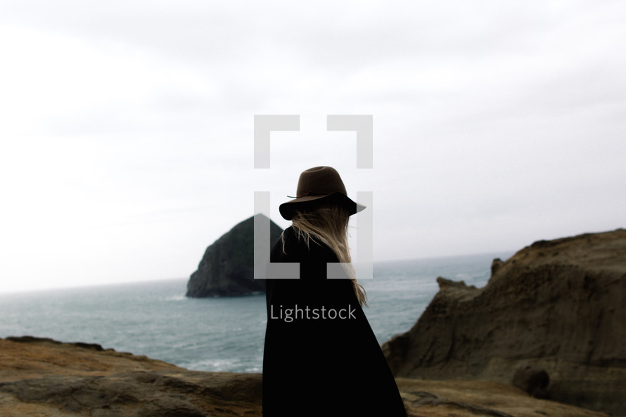 woman in a hat standing between rocks on a beach 