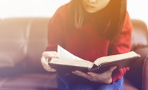 a woman reading a Bible sitting on a couch 