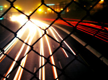 looking through a fence at the lights from moving cars at night
