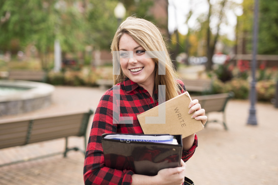 a young woman on campus holding a notebook and journal 