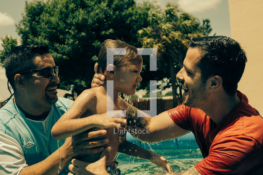 Two pastors raising a little boy from baptismal waters.