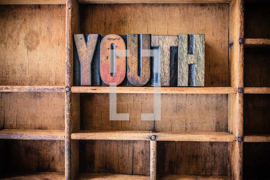 Wooden letters spelling "youth" on a wooden bookshelf.