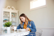 a woman reading a Bible sitting at a kitchen table 