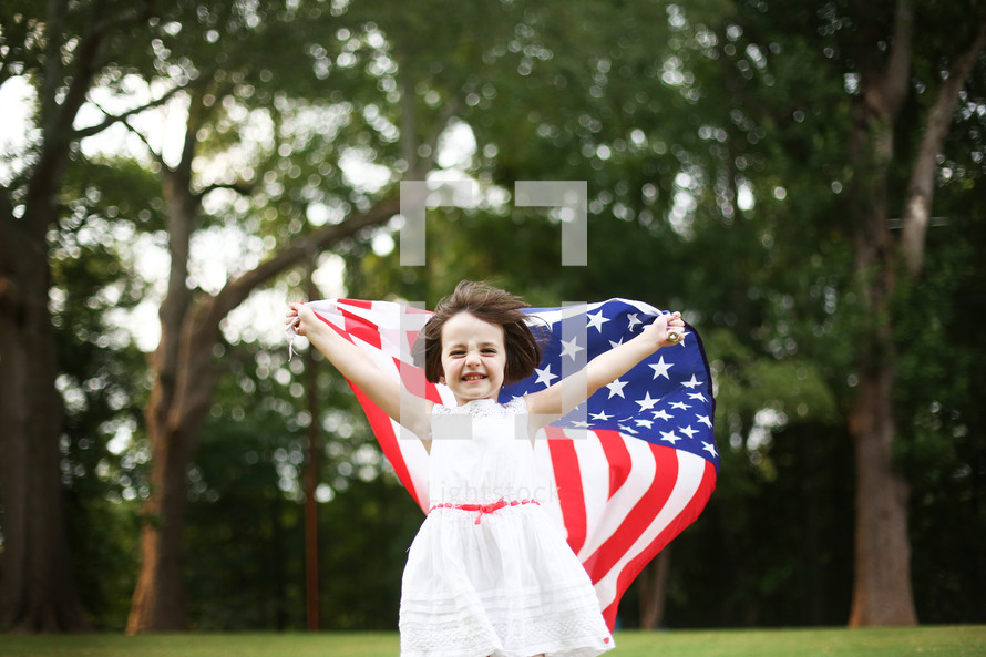girl child in a white dress holding up an American flag 