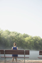 Woman sitting on a park bench in the morning mist.  