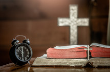 silver cross in front of a Bible and alarm clock 