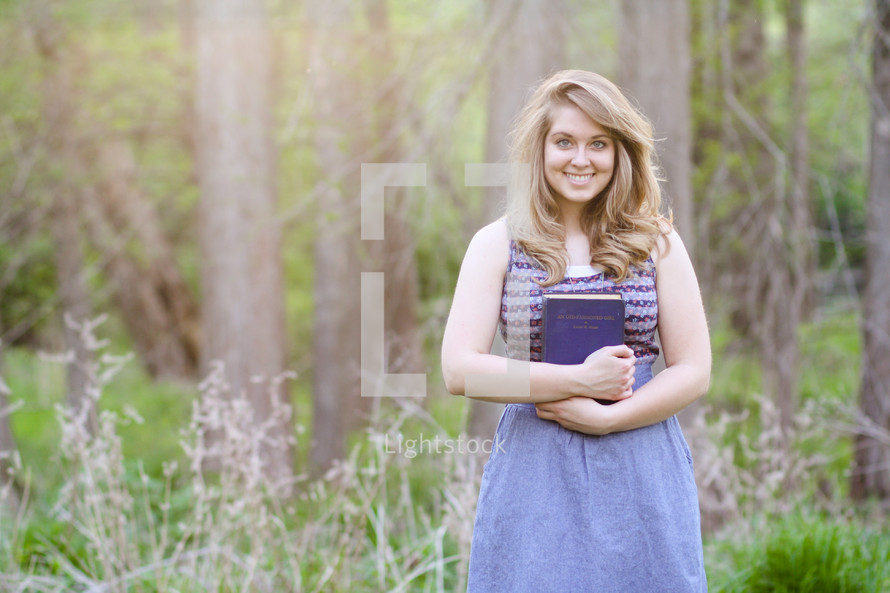 s young woman holding a Bible standing in a forest 