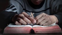a man with a cross and hands in prayer over a Bible 