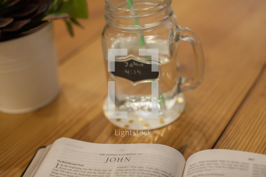 A cup of water with John 4:14 written on it and an open Bible