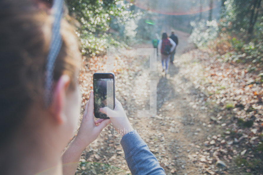 woman taking a picture with her cellphone of a group hiking on a nature trail 