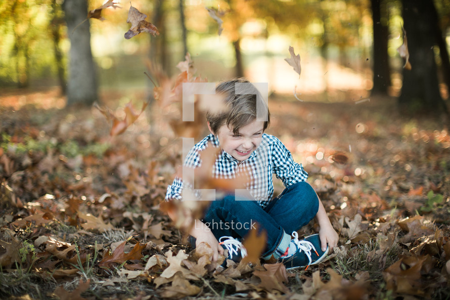 a boy child sitting in fall leaves 