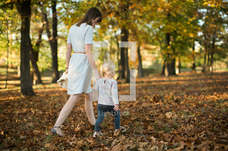 mother and toddler daughter walking through fall leaves 