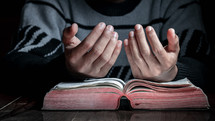 a male with lifted hands over a Bible in prayer 