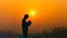 silhouette of a boy praying outdoors at sunset 