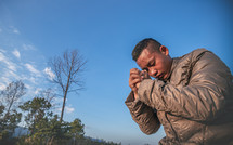 a man praying outdoors in a coat 