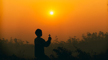 a male holding a cross at sunset against an orange sky