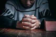 A man praying next to a closed Bible 
