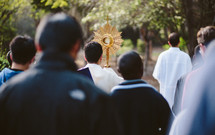 Priest and a crowd walking during a Catholic Eucharistic procession with a monstrance. 