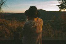a woman with a hat looking out at mountains 