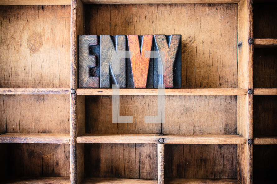 Wooden letters spelling "envy" on a wooden bookshelf.