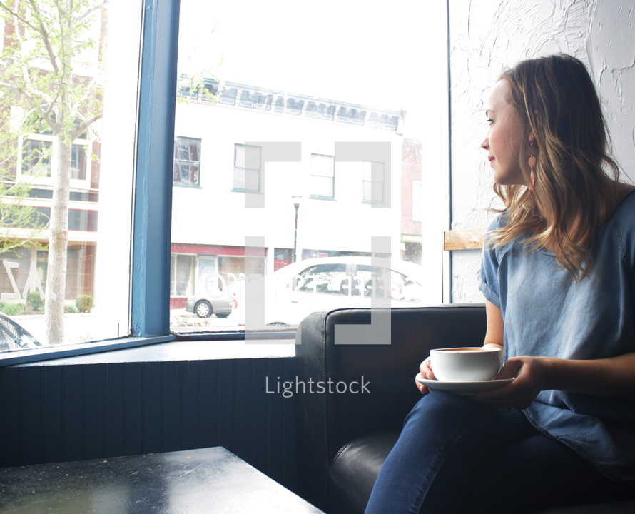 a woman with a coffee cup looking out a window 