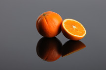 A whole orange and a sliced orange and their reflections.