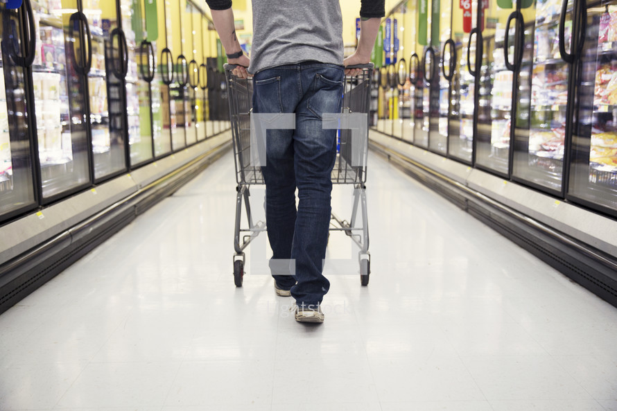 a man pushing a shopping cart through a grocery store isle.