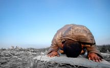 a man kneeling in praying on a rug outdoors 