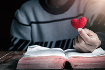 a man holding a red felt heart over the pages of a Bible 