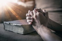 a man's praying hands over a Bible 