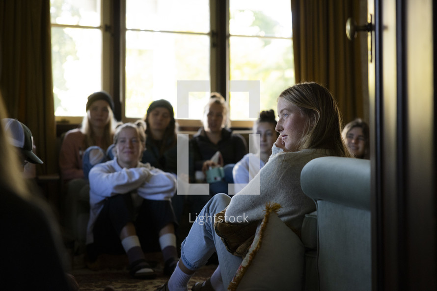 a close up of a young woman listening in a group of young people inside a room filled with natural light
