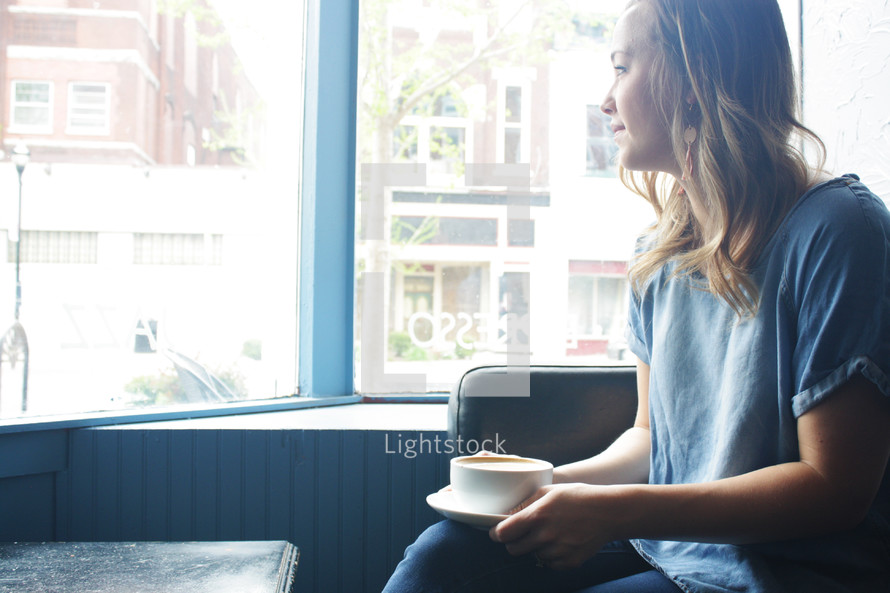 a woman with a coffee cup looking out a window 