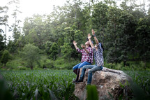Two young male hands raised and praying in corn field.