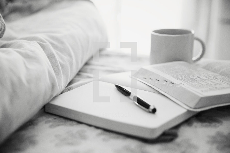 journal, pen, Bible, and coffee mug on a bed 