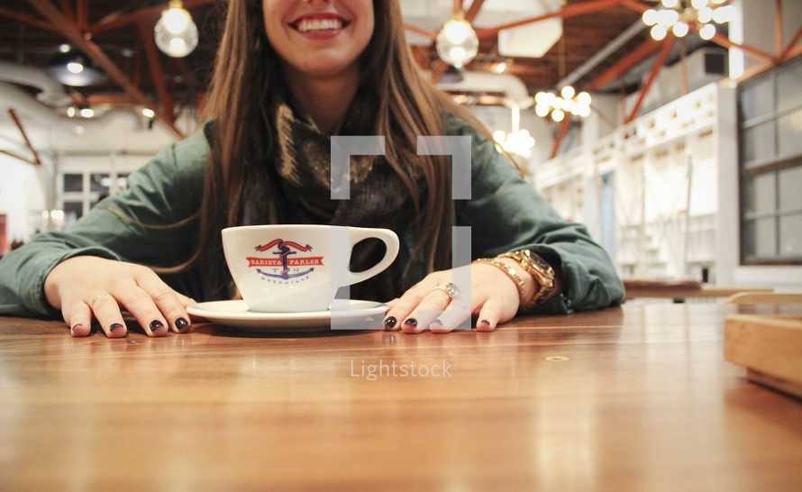 woman with hands on a table in front of a coffee cup 