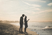 a man and woman standing on a beach at sunrise 