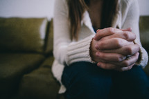 A woman sits with her hands clasped together.