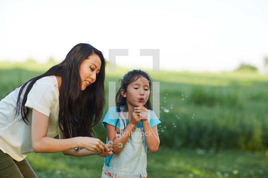 mother and daughter blowing dandelions 