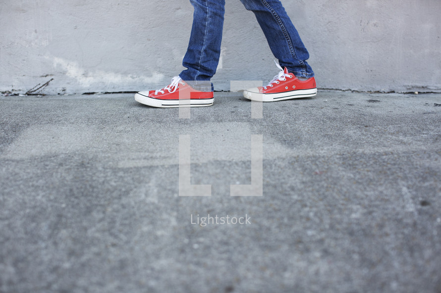 a boy child in sneakers walking on a sidewalk 