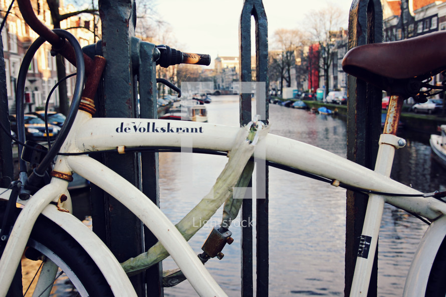 A bicycle parked on the edge of a canal in the middle of a city.