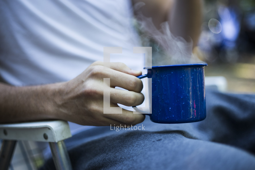 man in a folding chair holding a steaming cup of coffee